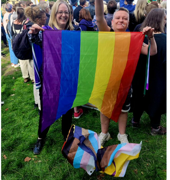 Helen Joyce holding a torn LGBT+ Progress Flag with the section representing the trans community torn out and being trod on. 